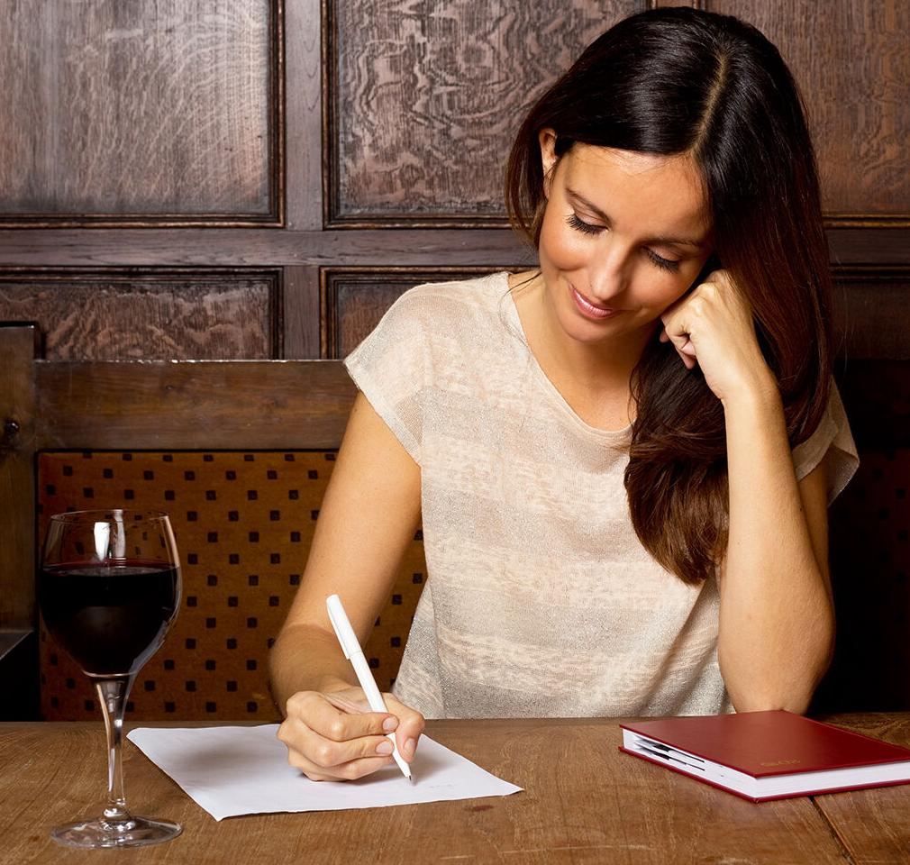 young woman writing with a glass of wine.